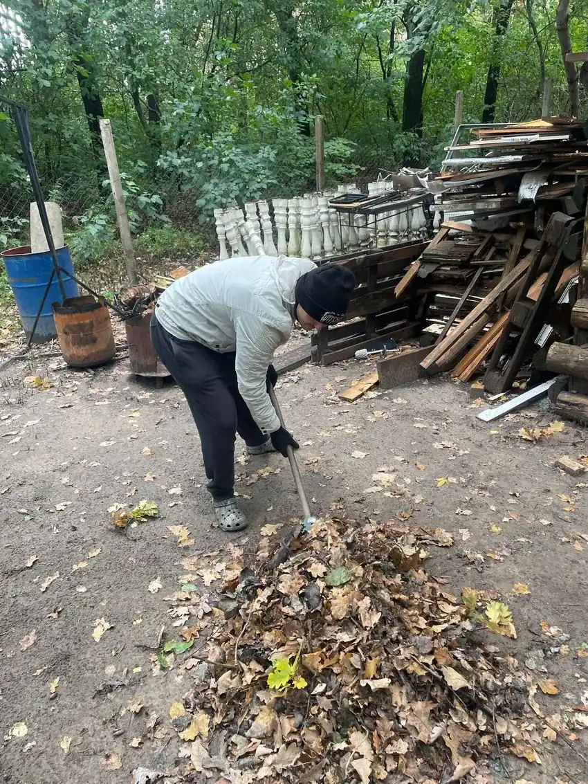 Паша згрібає листя біля дровʼяника